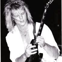 Black-and-white photo of a long-haired guitarist in a white shirt, late 1980s