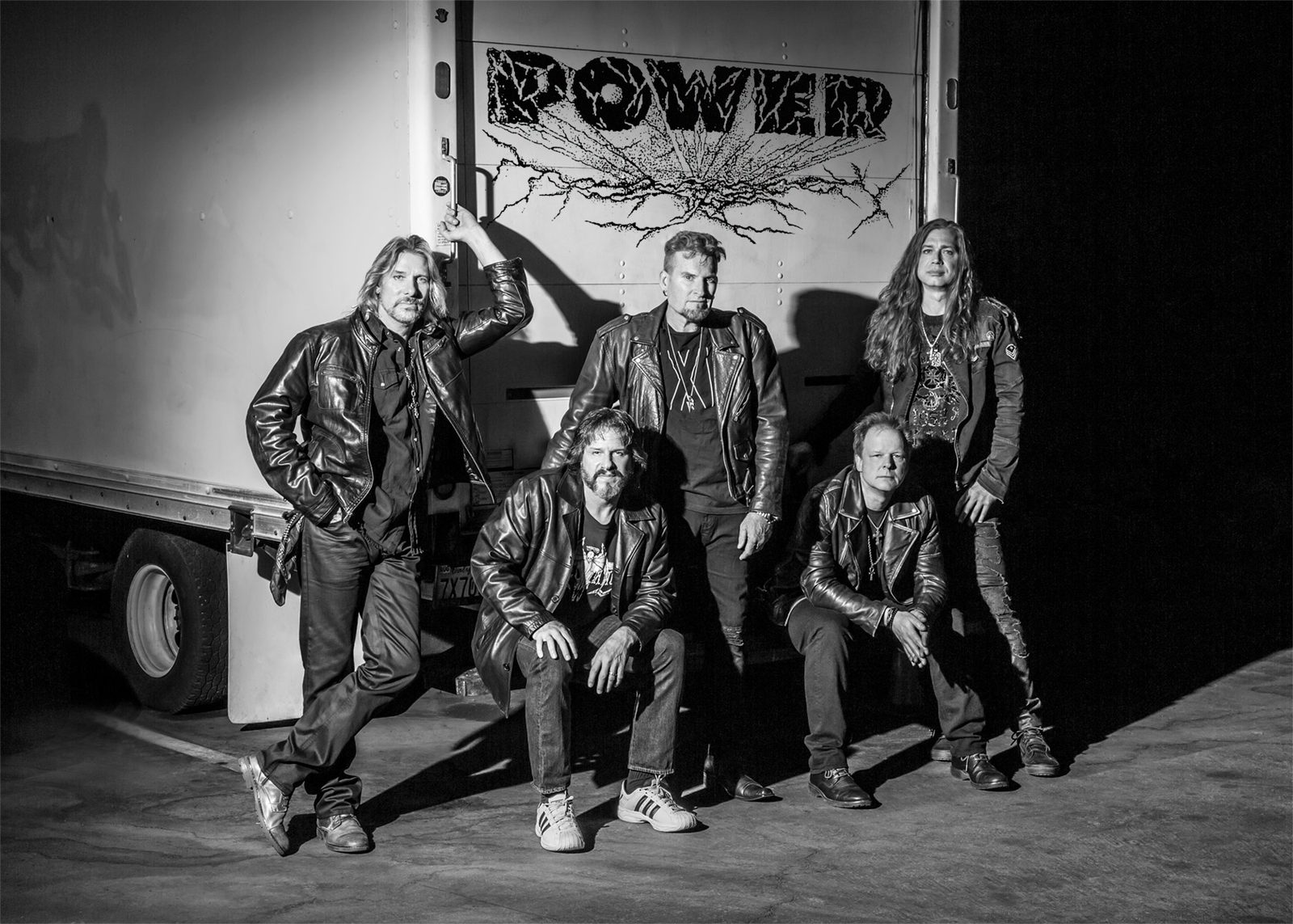 The five members of POWER in leather jackets, posed in front of a truck painted with the POWER logo